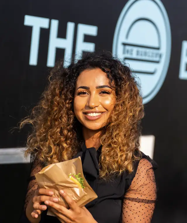 Smilende gæst med en frisklavet burger foran The Burgerys foodtruck